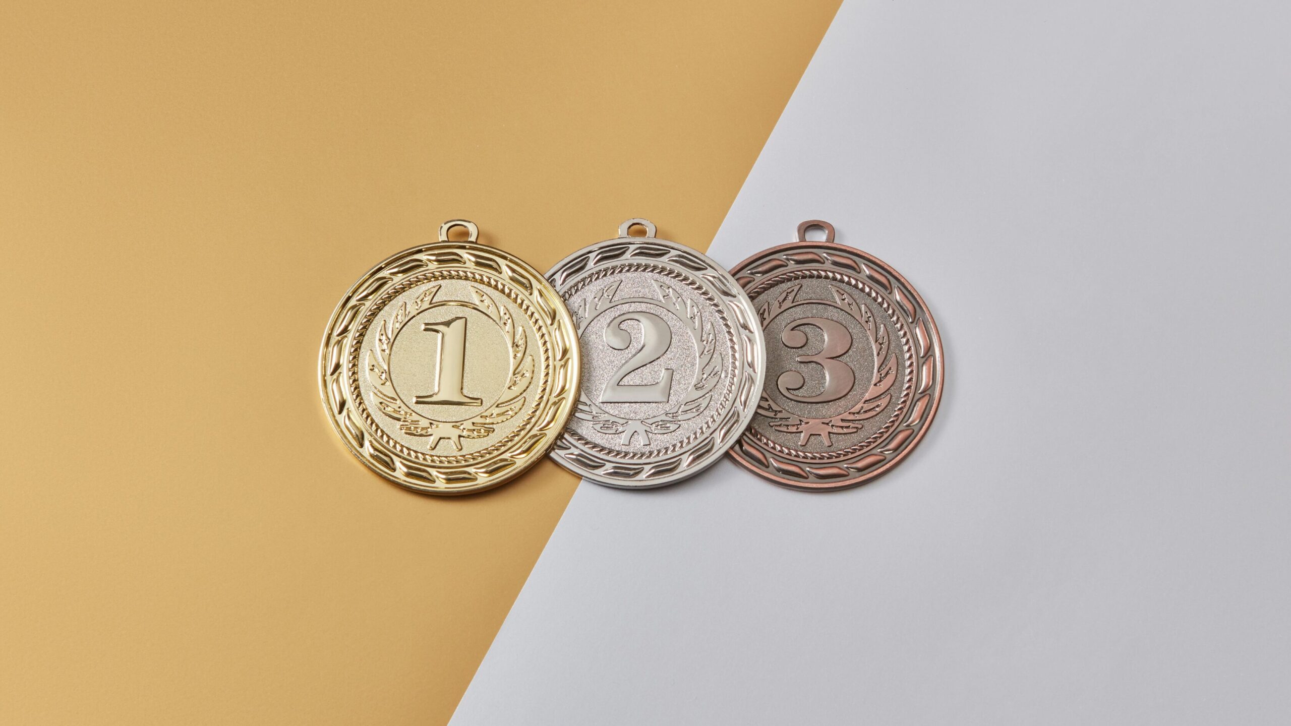 Gold, silver, and bronze medals labeled 1, 2, and 3 placed side by side on a split gold and gray background, symbolizing sponsorship tiers or ranking levels.